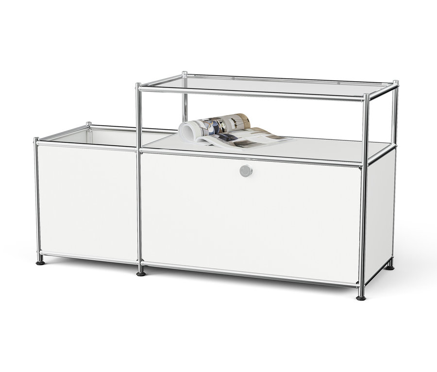 Bílý modulární úložný systém s chromovaným rámem a skleněnými policemi, na horní polici je srolovaný časopis.