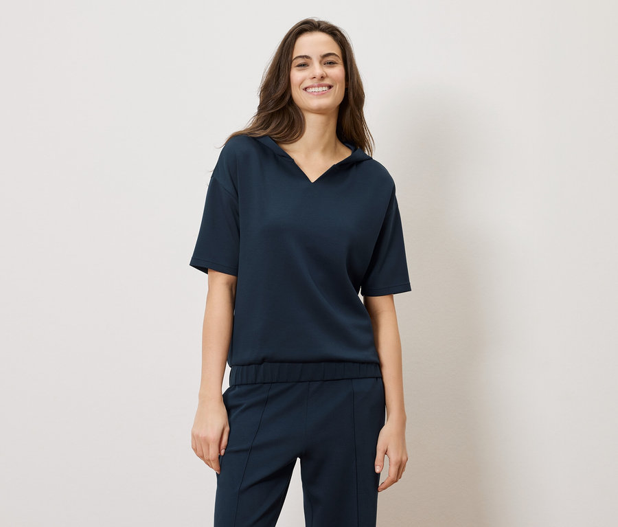 Usmívající se brunetka má na sobě tmavě modrý komplet: halenku s krátkým rukávem a kalhoty.