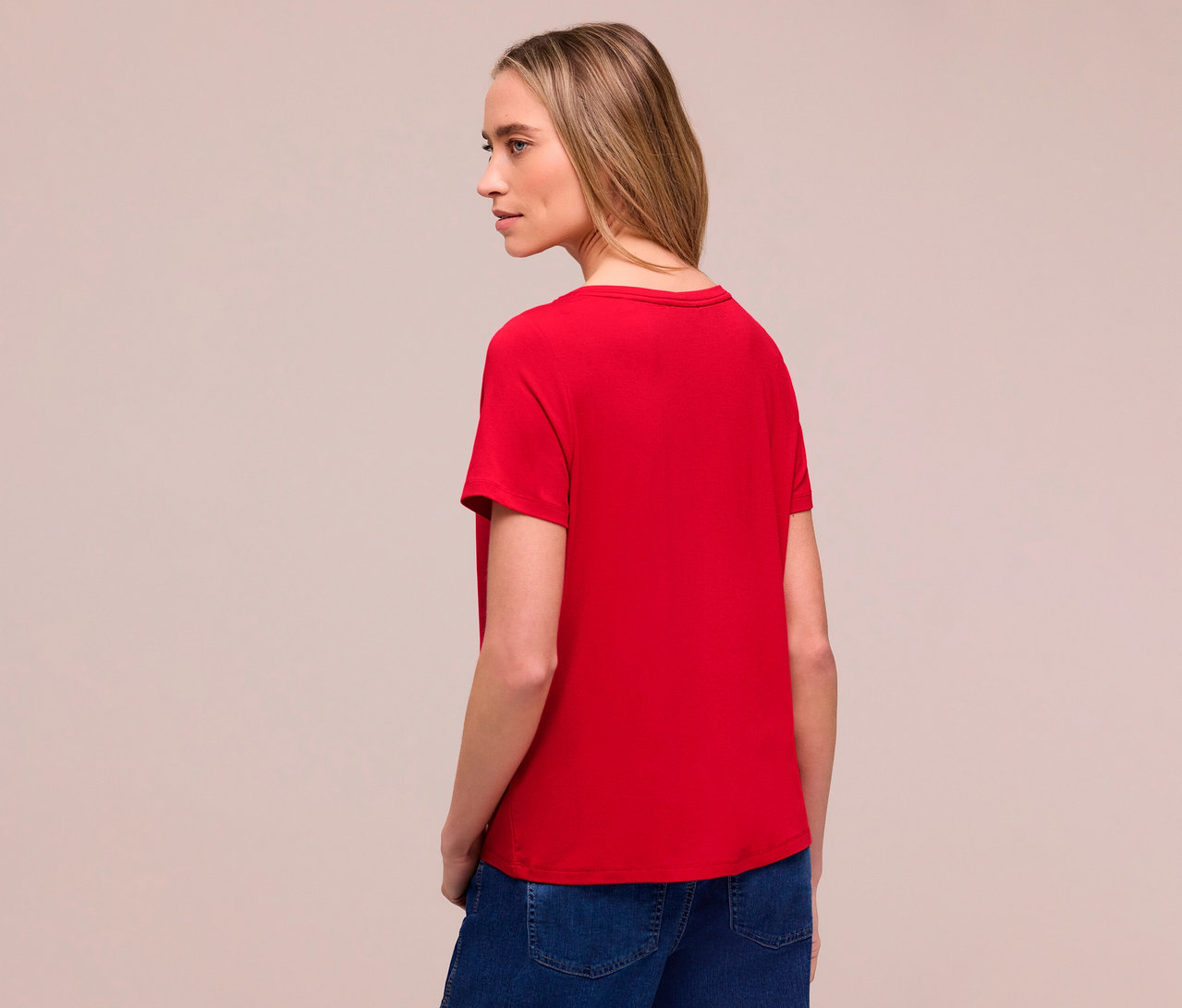 Žena zezadu v červeném tričku Street One a džínách. Dívá se doleva.
