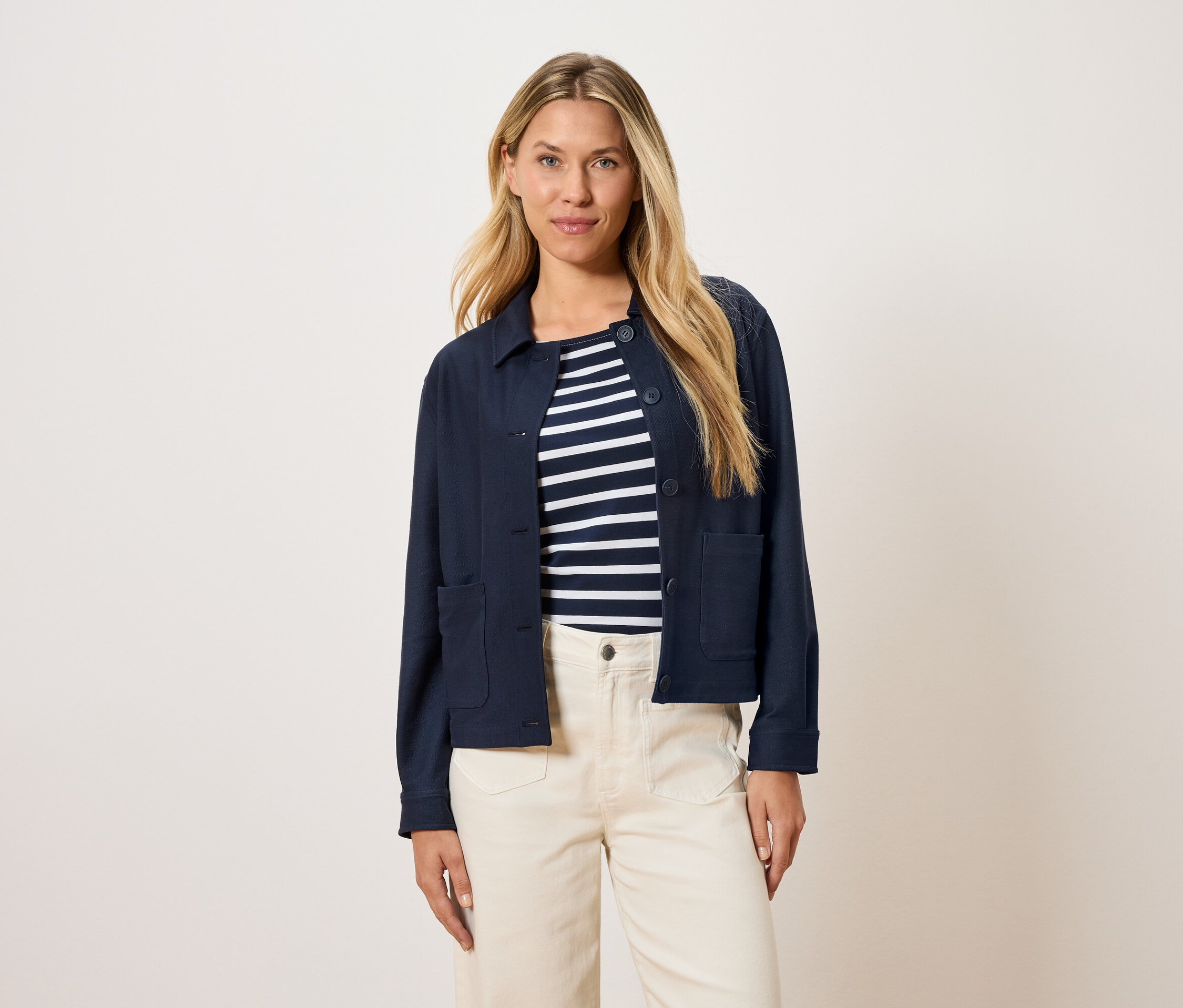 Žena má na sobě tmavě modrou bundu přes pruhovaný top a krémové kalhoty.