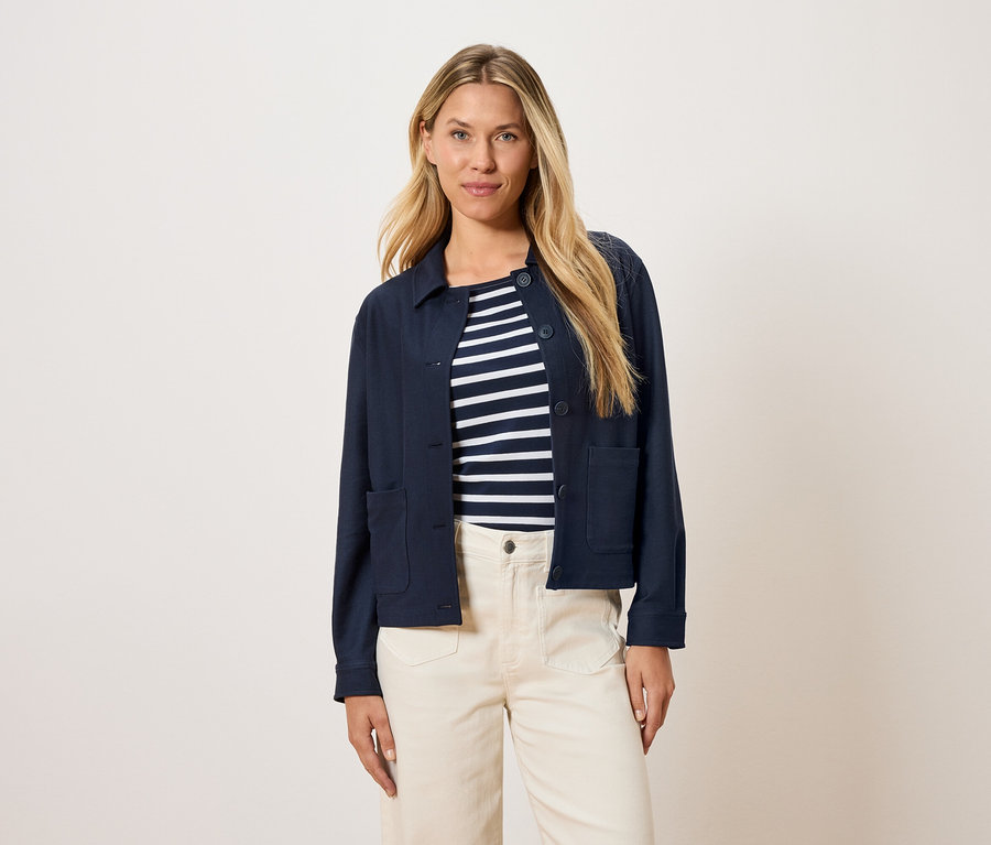 Žena má na sobě tmavě modrou bundu přes pruhovaný top a krémové kalhoty.