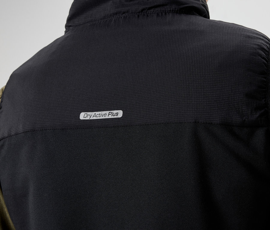 Detailní záběr na zadní část černé vesty s nápisem "Dry Active Plus" oblečené na olivově zelené košili s dlouhým rukávem.