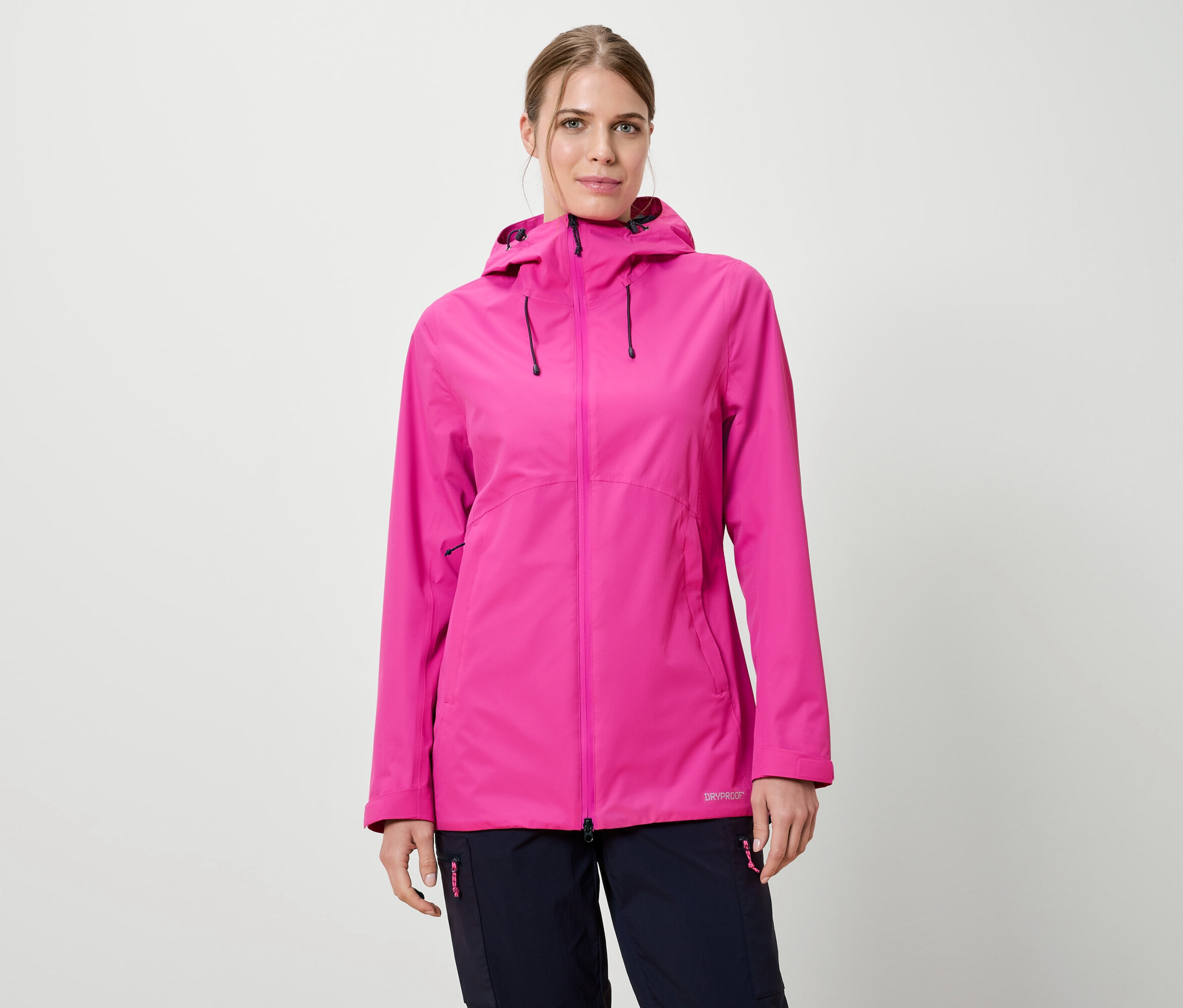 Žena má na sobě růžovou pláštěnku s kapucí a tmavě modré kalhoty na bílém pozadí.