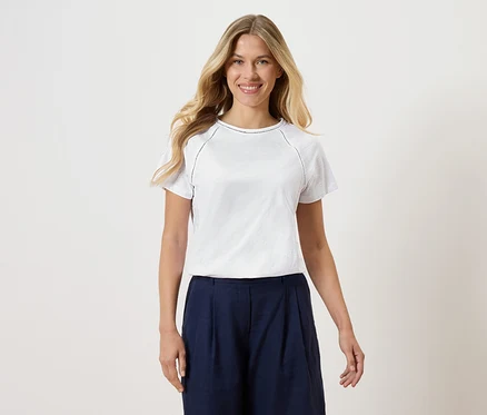 Žena má na sobě bílé tričko a tmavě modré culottes na bílém pozadí.