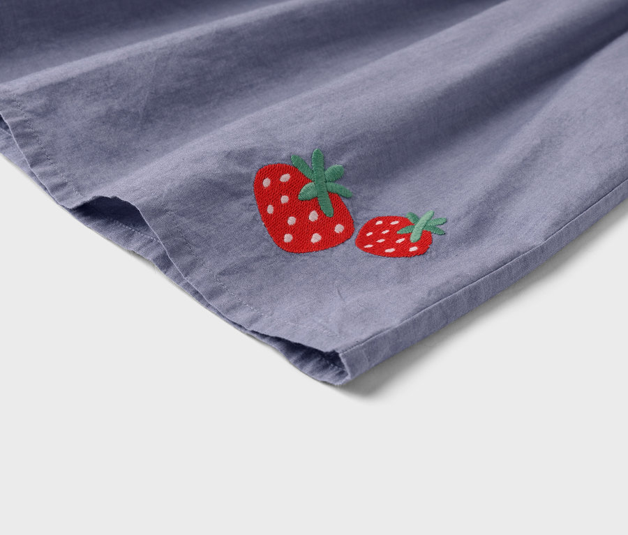 Detailní pohled na fialovou látku se dvěma vyšitými jahodami.