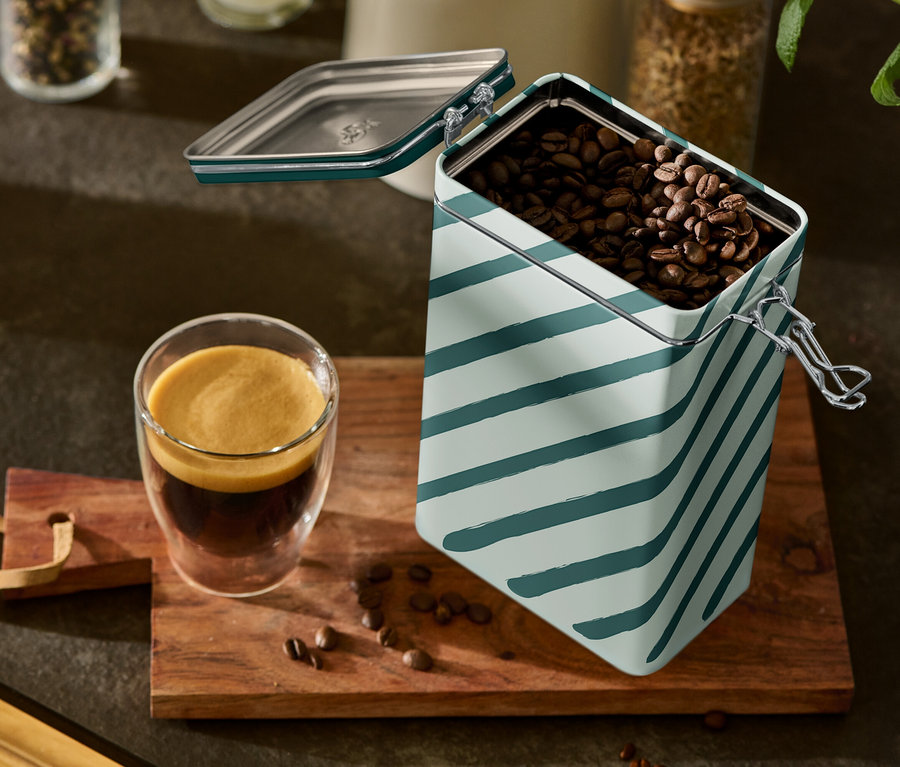 Sklenice espresa a otevřená, pruhovaná dóza na kávu stojí na dřevěné desce.