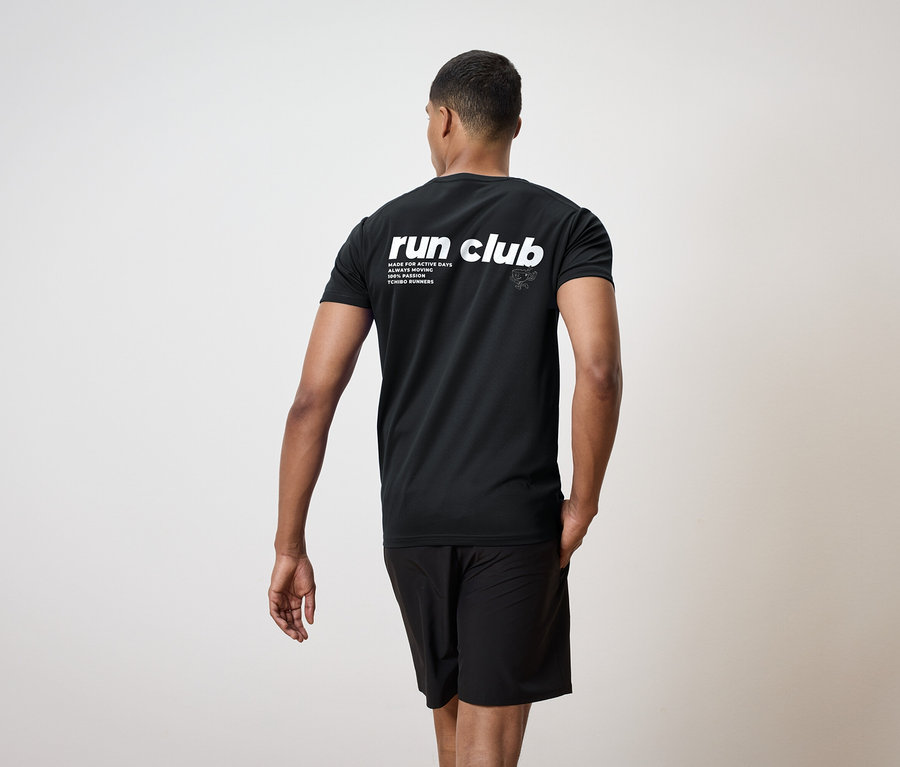 Muž zezadu, oblečený v černém tričku s nápisem "run club" a černých šortkách.