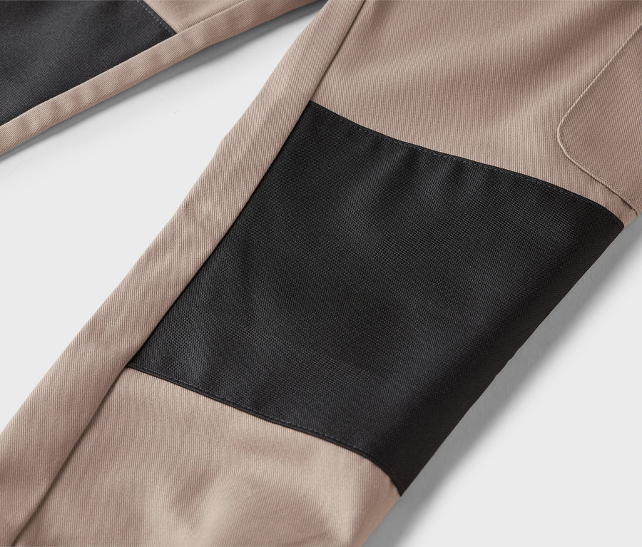 Detail béžových kalhot s černými záplatami.