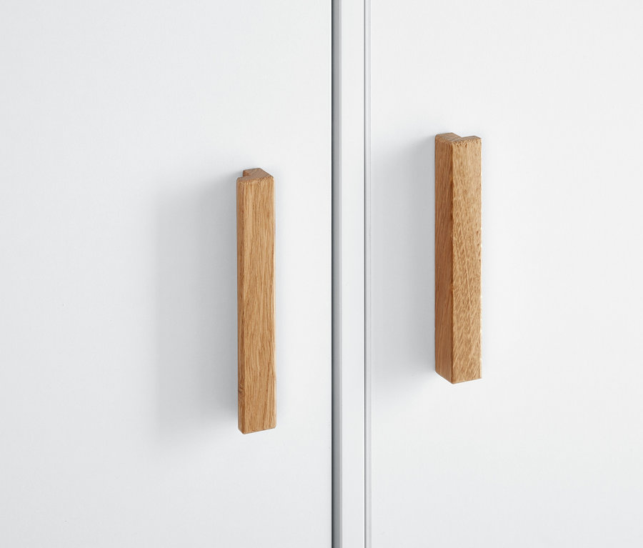 Detail bílé šatní skříně s dřevěnými úchyty.