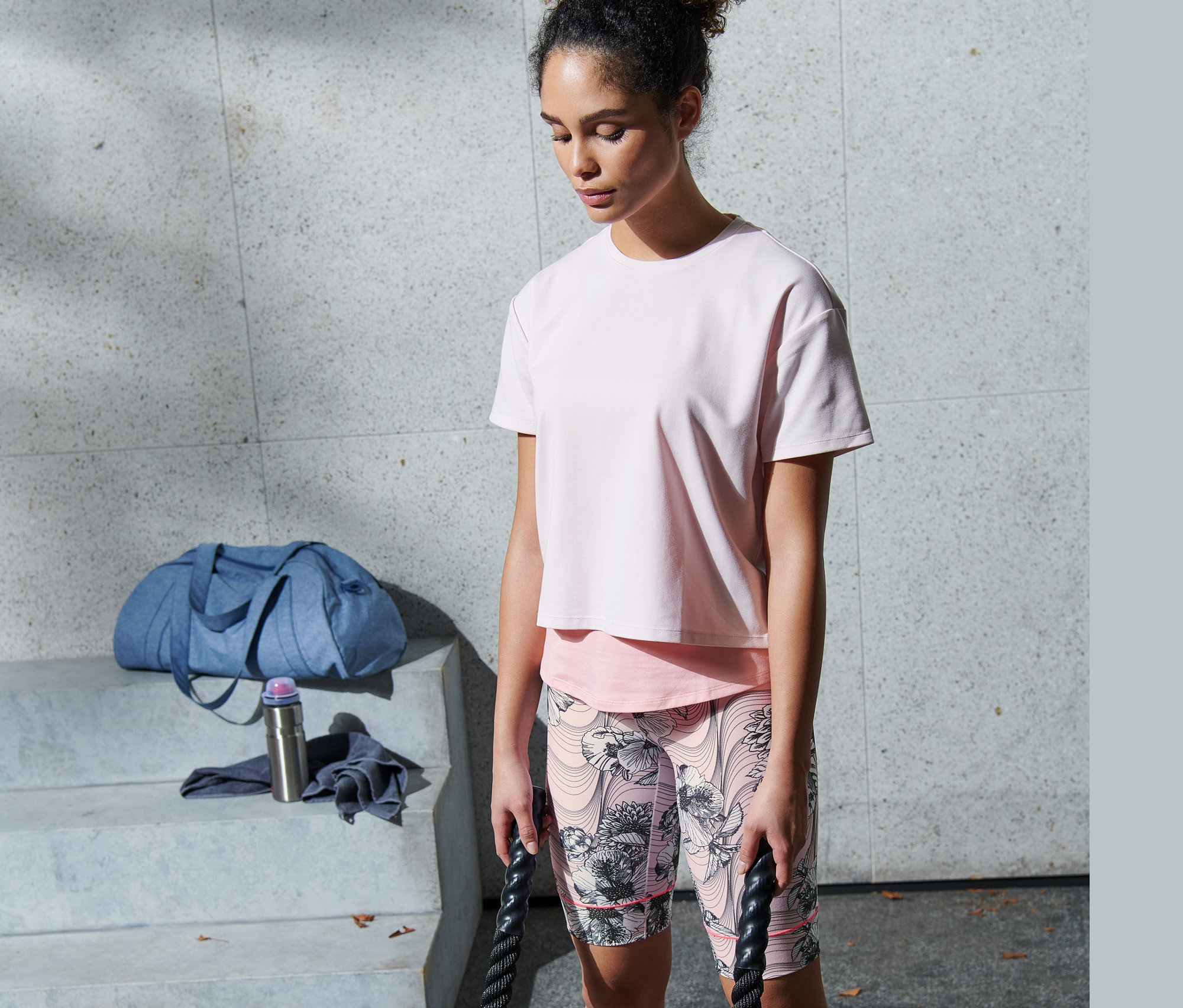 Žena cvičí s lany v růžových funkčních cyklistických kalhotách.