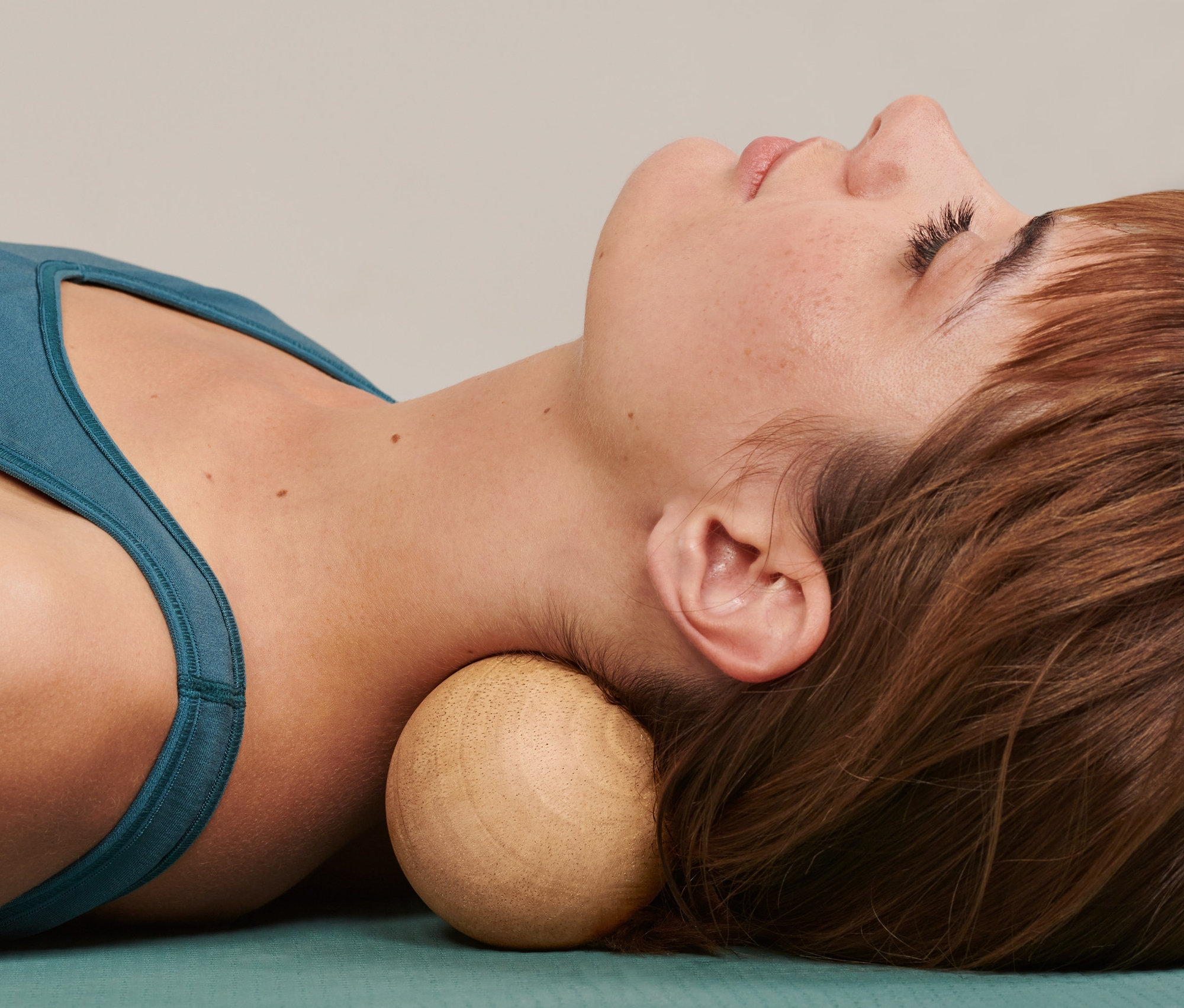 Žena leží na podložce a pod krkem má dřevěný dvojitý masážní míček.