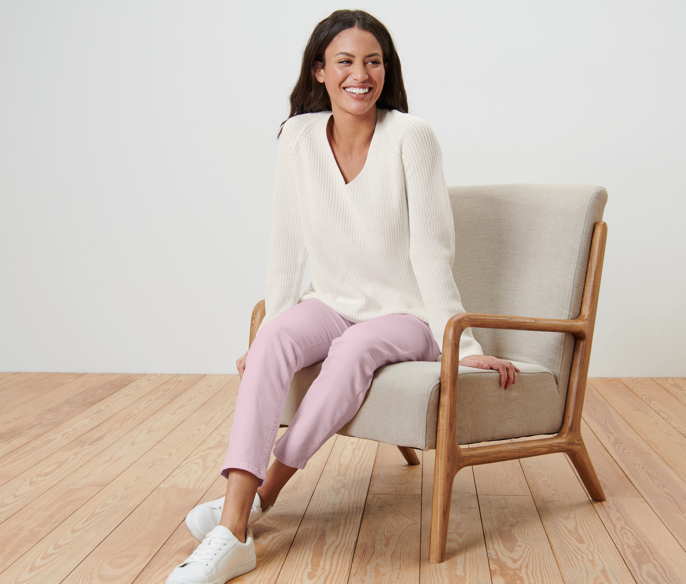 Žena sedí v křesle a má na sobě krémový pletený svetr.