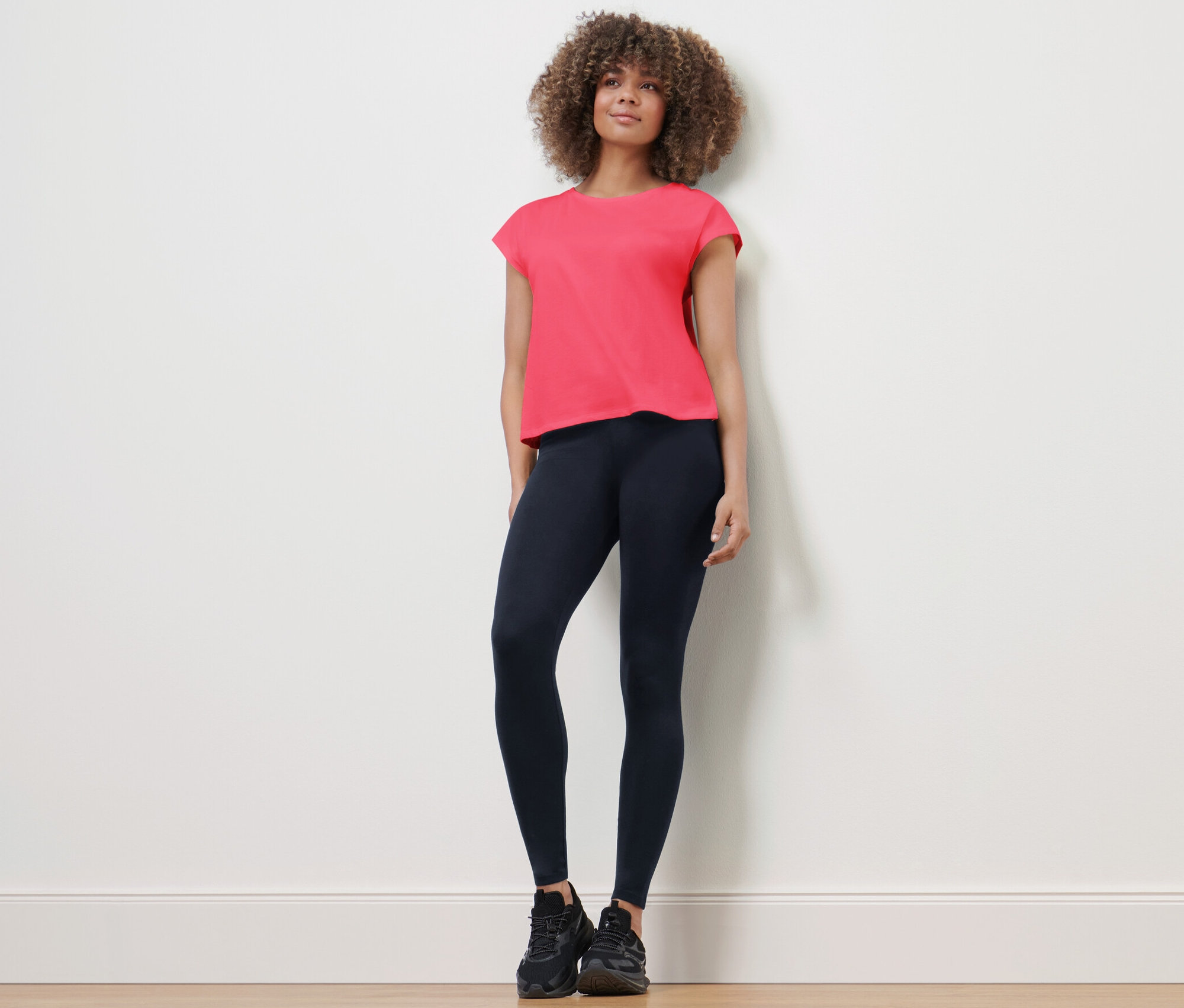 Žena stojí a má na sobě sportovní legíny a tričko.