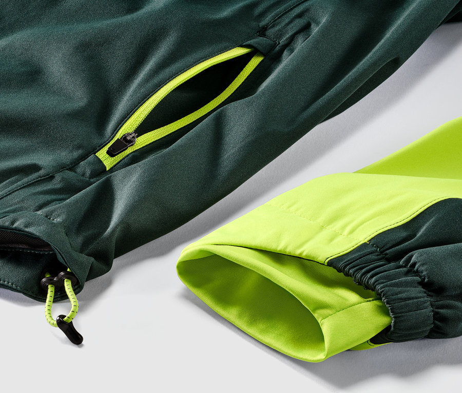 Detail cyklistické bundy do deště, která má zelenou barvu a neonově žlutý zip.