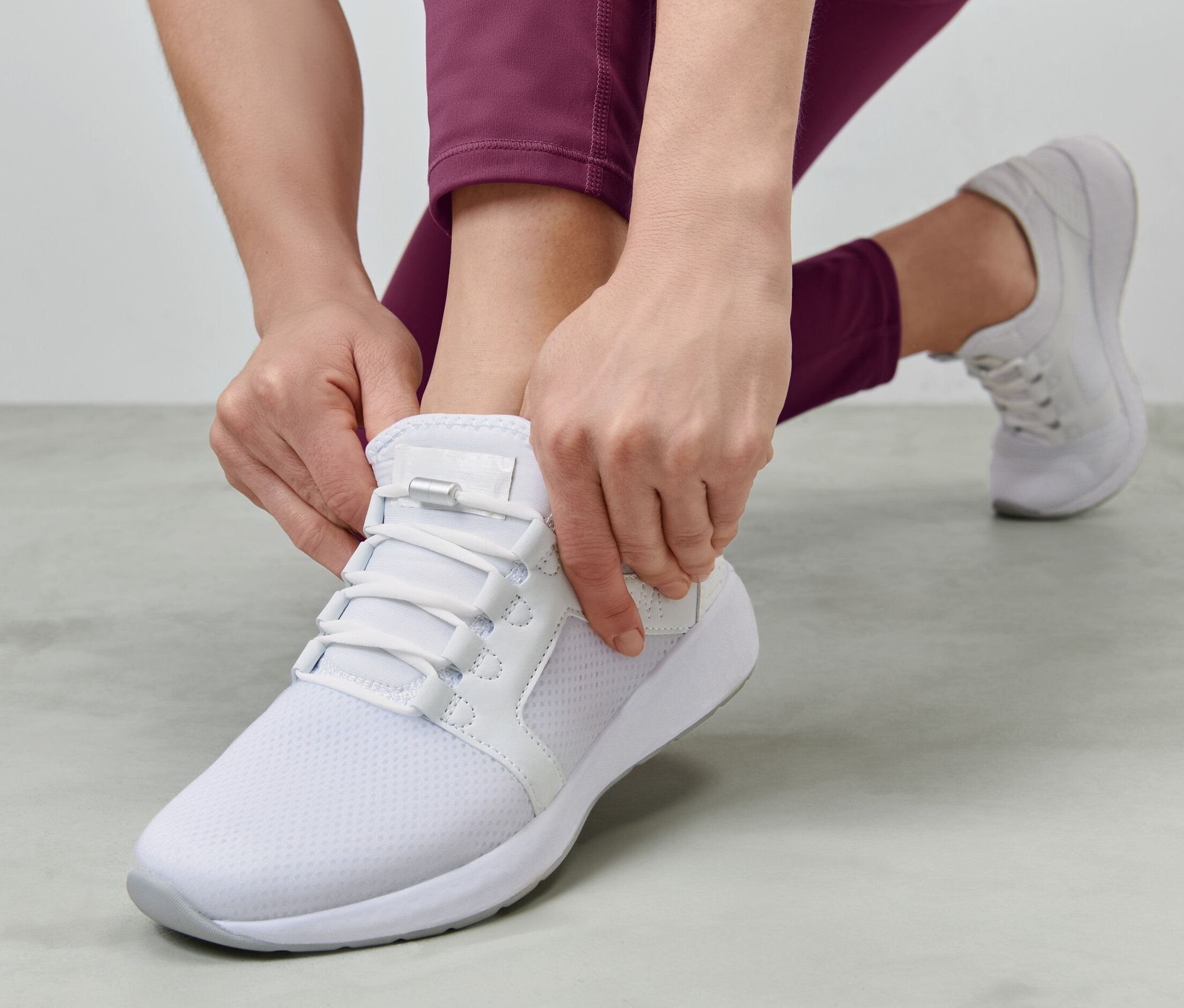 Žena si zavazuje elastické tkaničky na bílé botě.