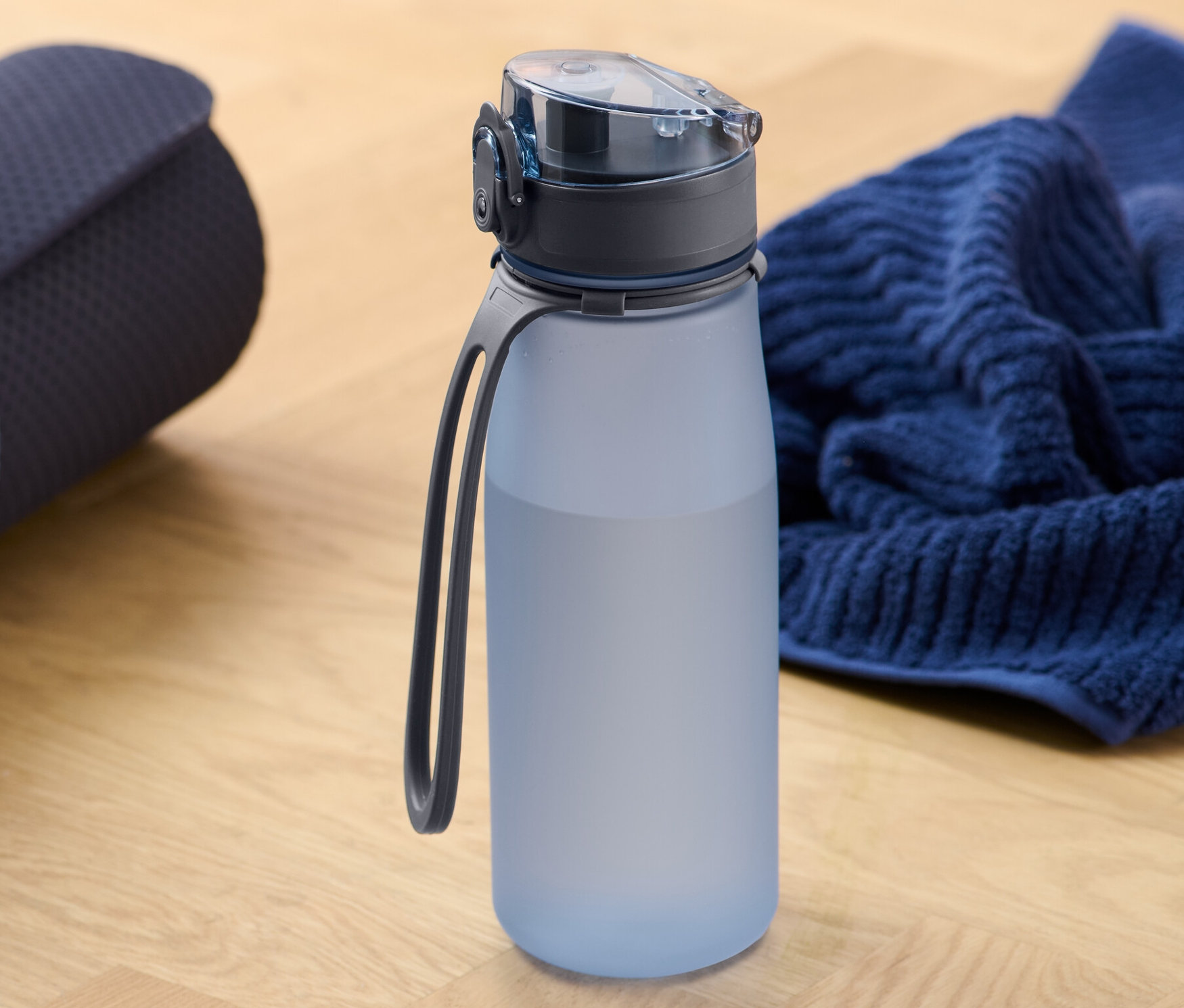 Srolovaná podložka na cvičení vedle sportovní láhve na pití a ručníku.