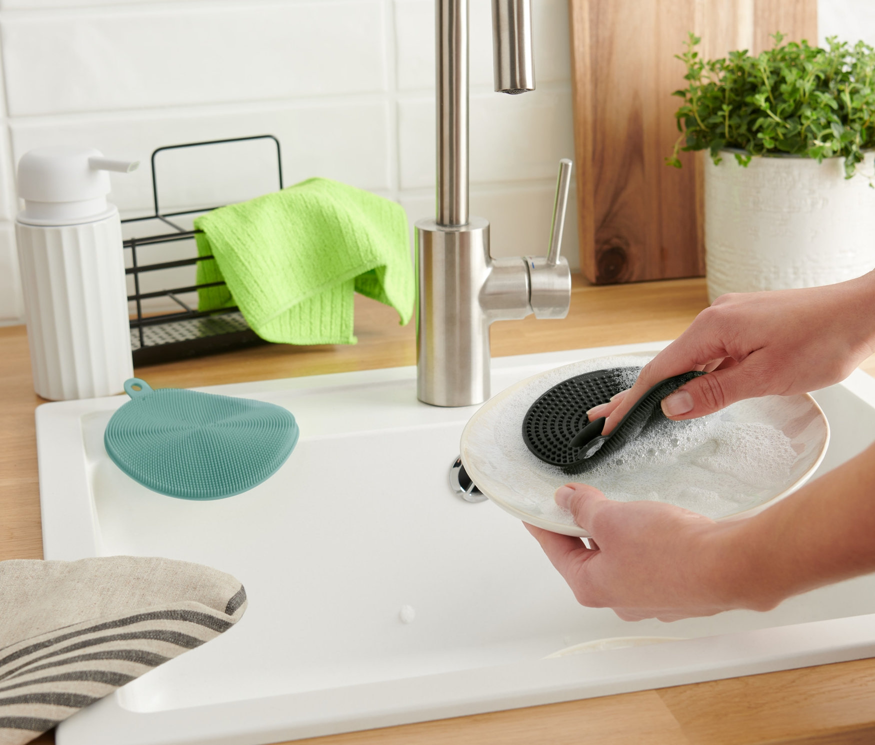 Žena myje talíř silikonovou houbičkou na nádobí (2 ks).