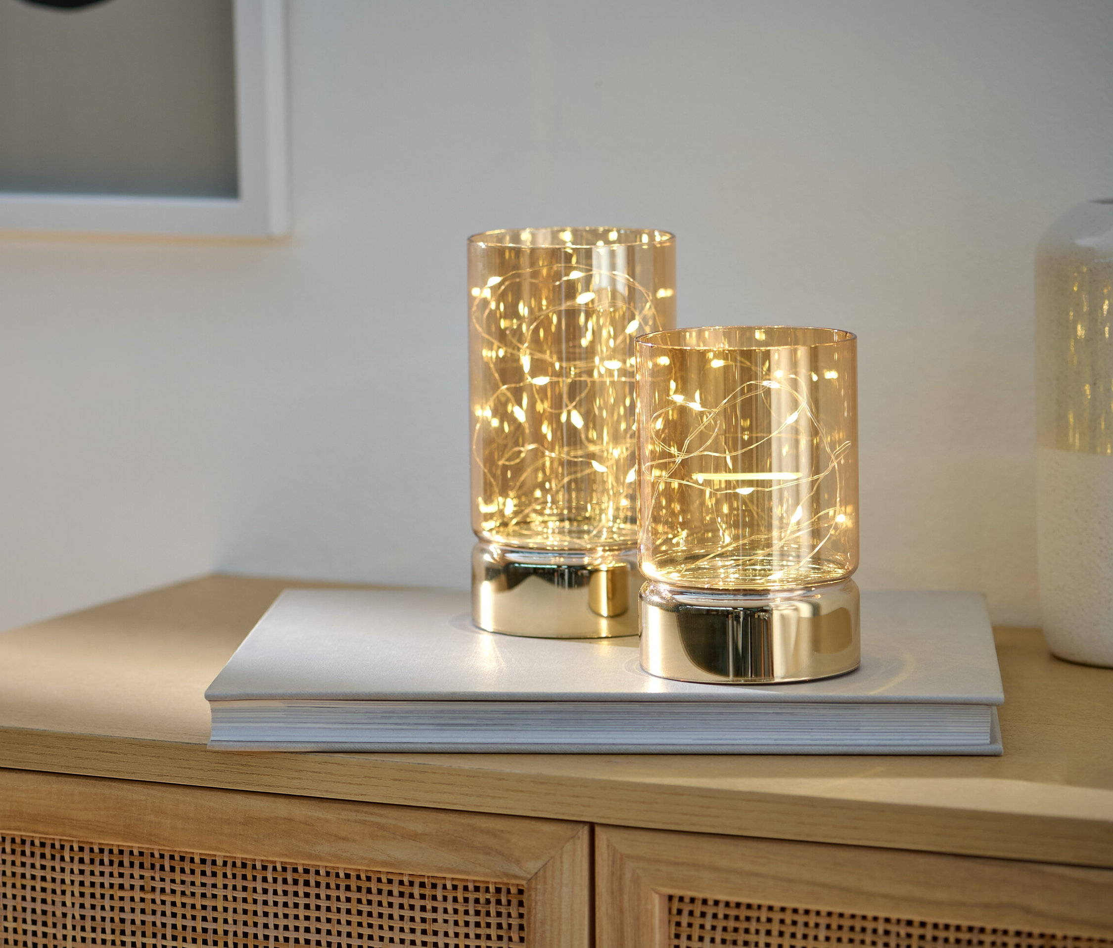 Dva LED svíčky ve skle stojí na knize na skříňce.