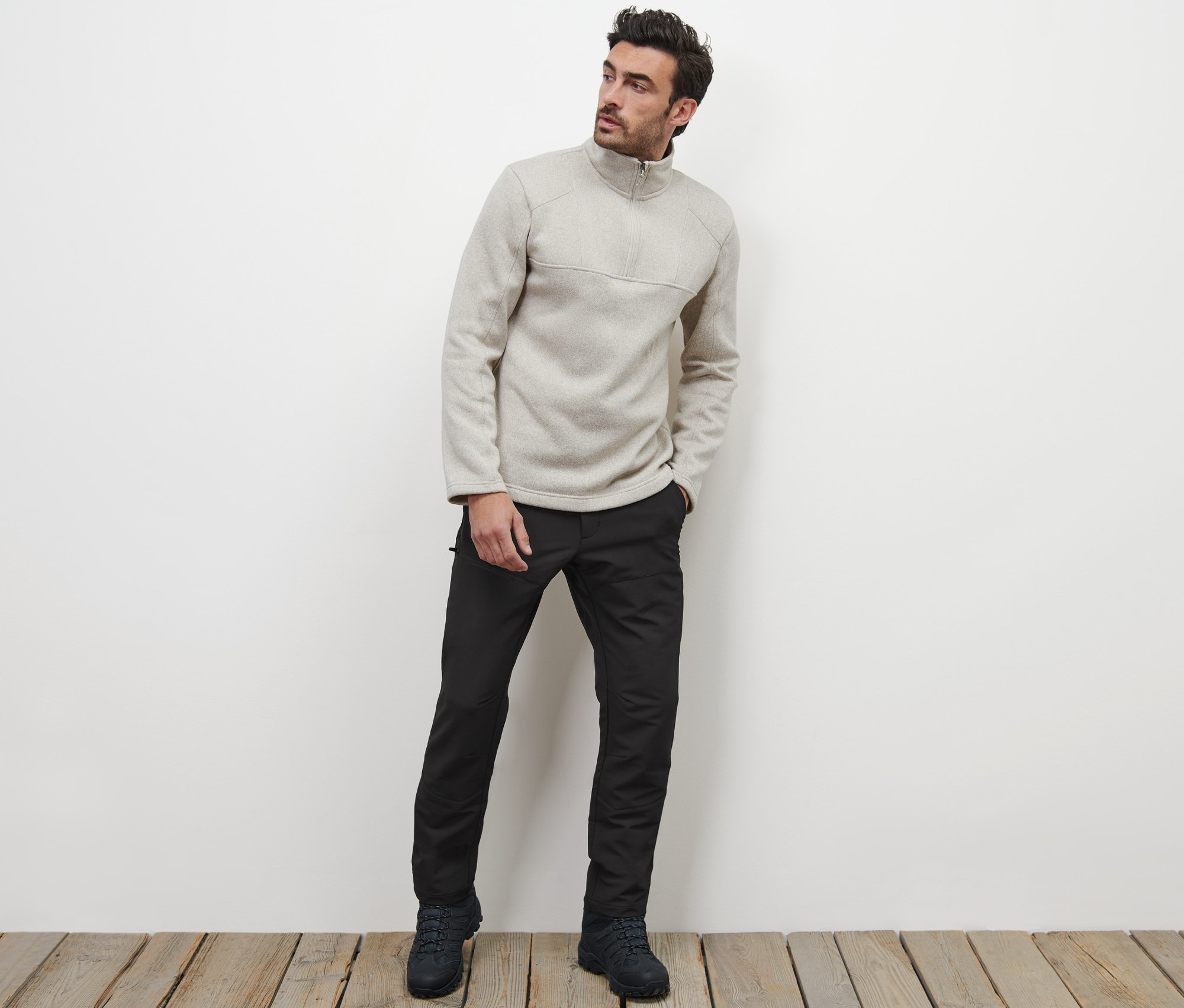 Muž pózuje na dřevěné podlaze a má na sobě termokalhoty a mikinu se zipem.