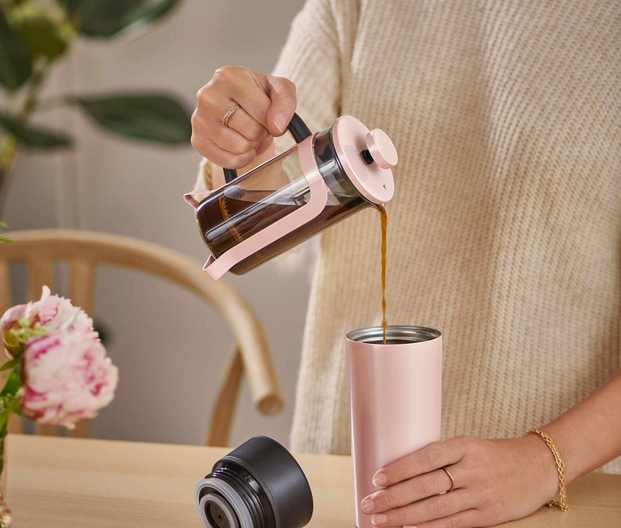 Žena nalévá kávu z french press konvice do cestovního hrnku.