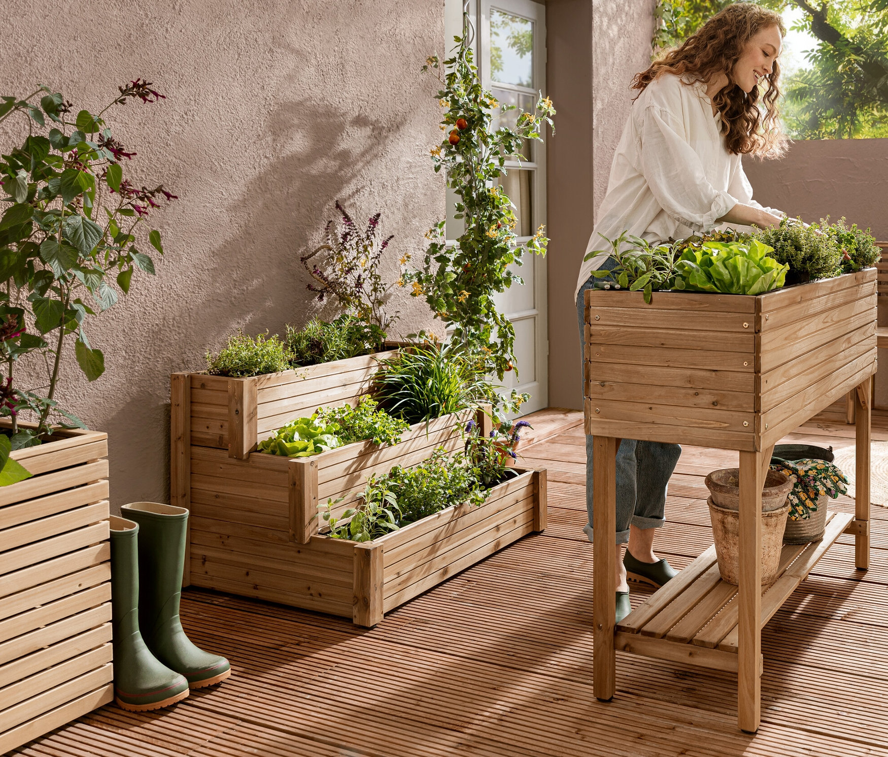 Žena pracuje na vyvýšeném truhlíku s policí »Tinus«. V pozadí je vidět vyvýšený schodový truhlík se 3 úrovněmi »Tinus«.