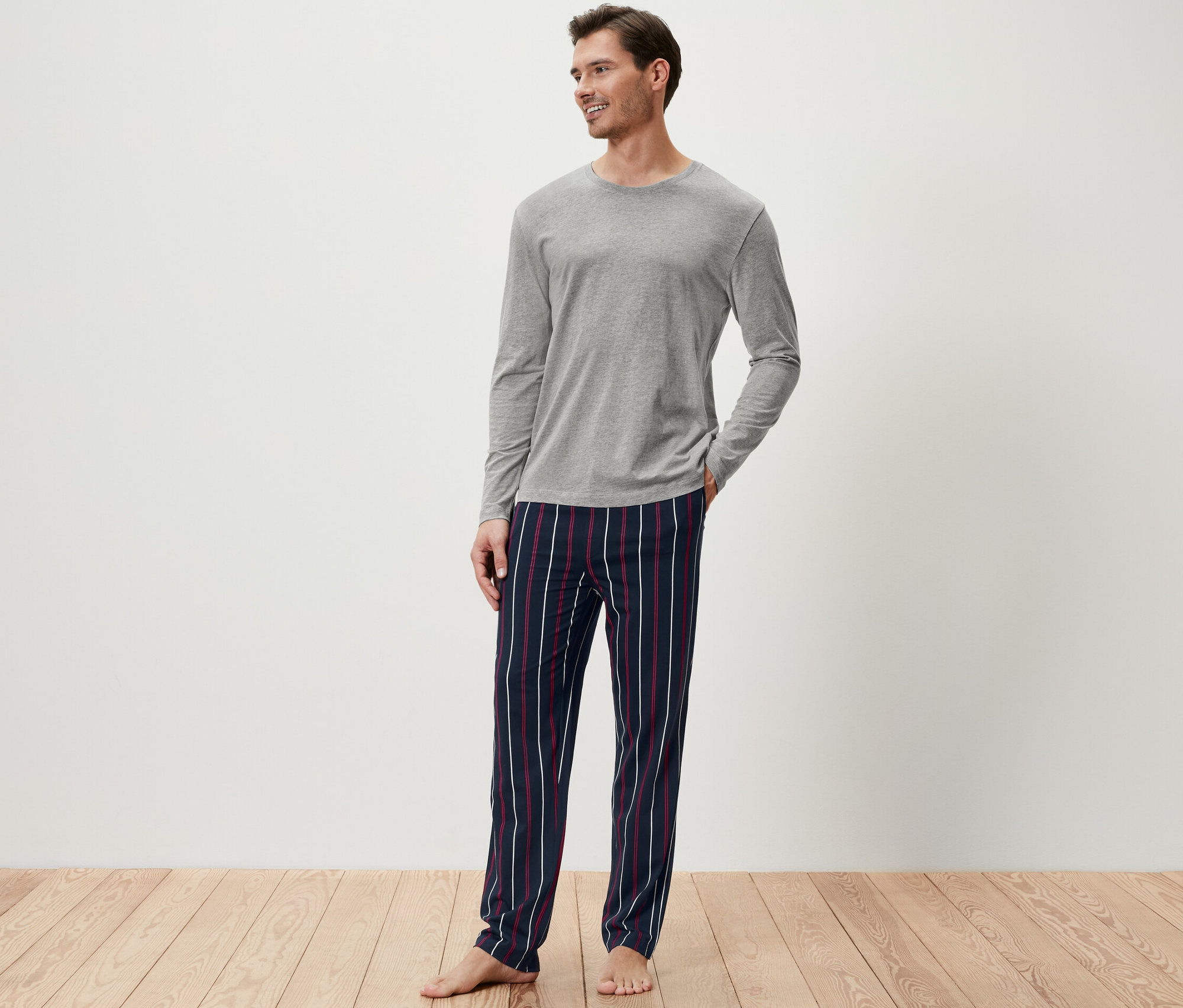Muž v šedém pyžamovém topu a pruhovaných pyžamových kalhotách.