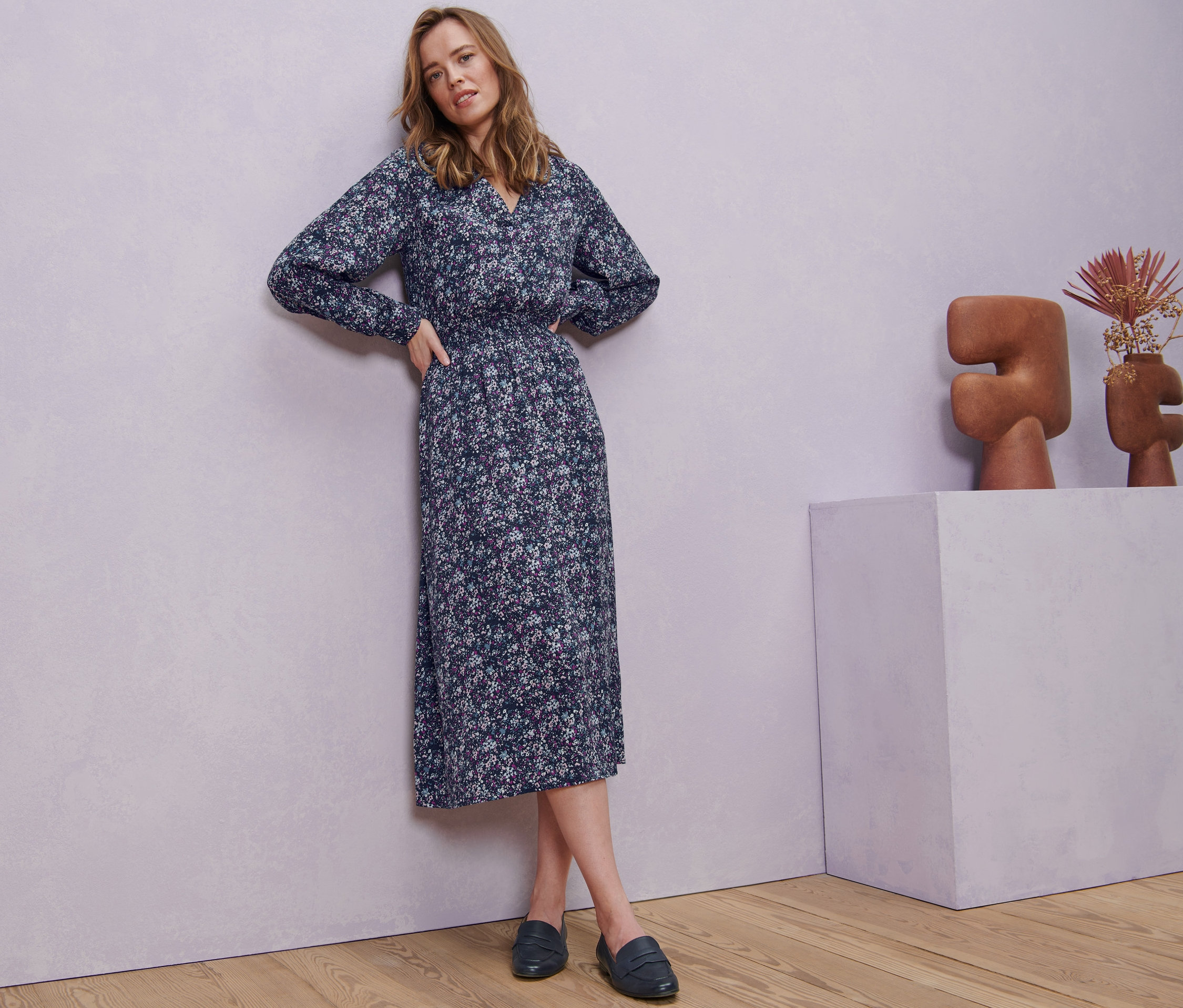 Žena pózuje v květovaných midi šatech.