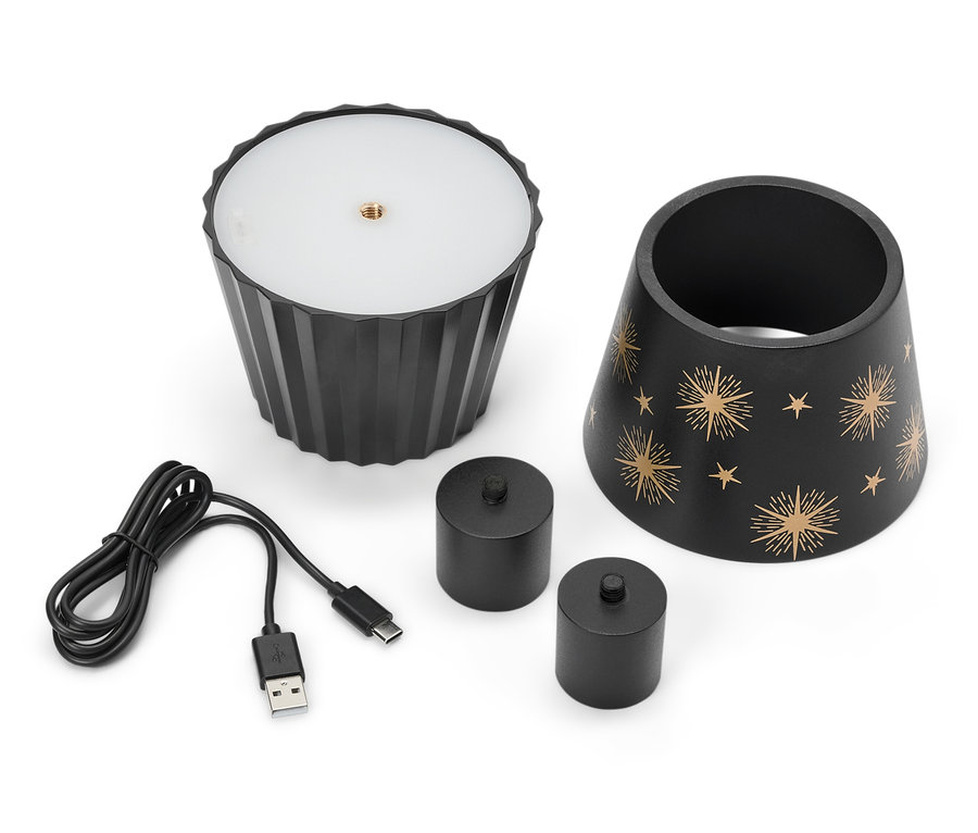 Černá lampa s hvězdami, dvě černé svíčky a USB kabel leží na bílém pozadí.