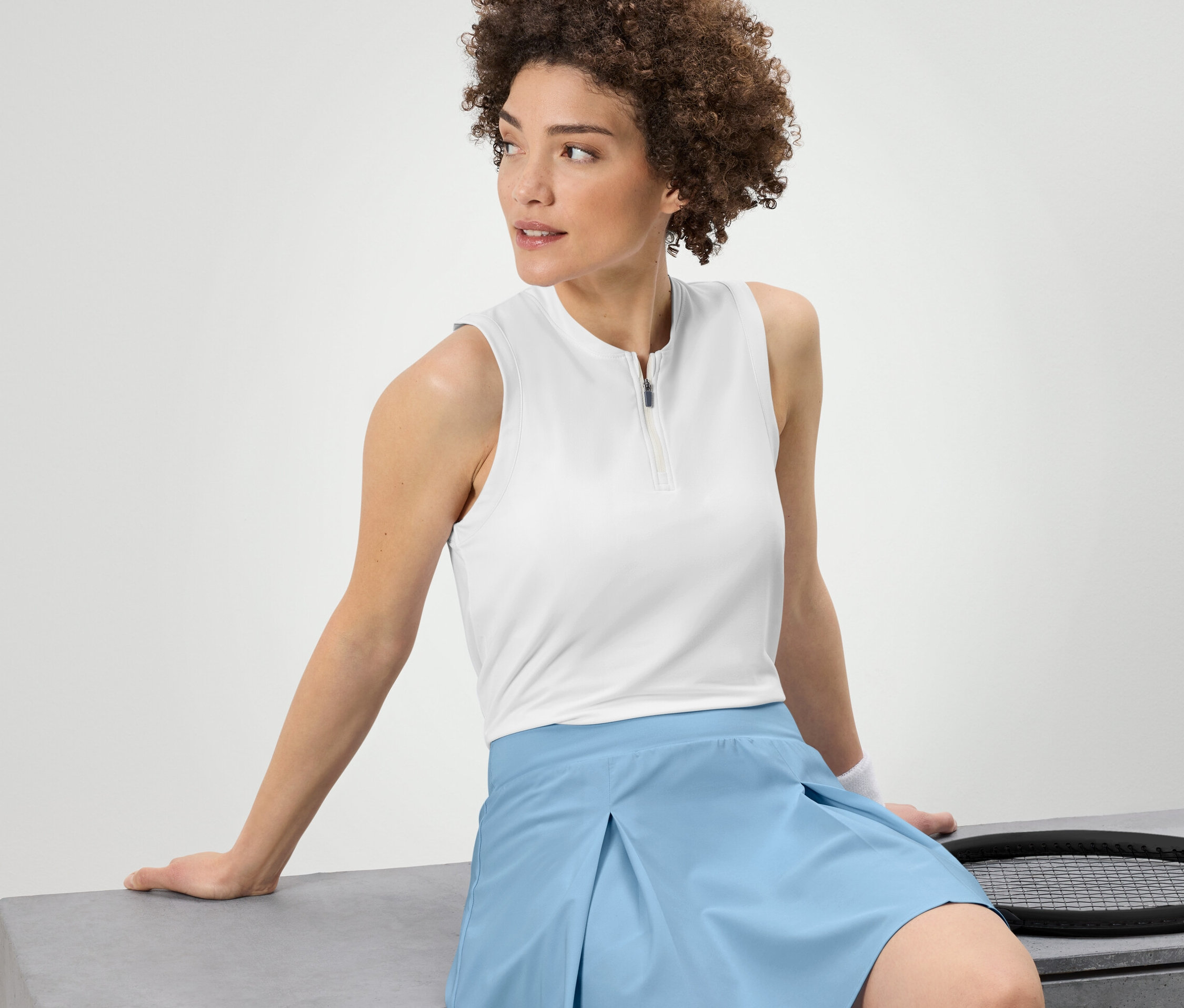 Žena sedí a má na sobě bílý funkční top.