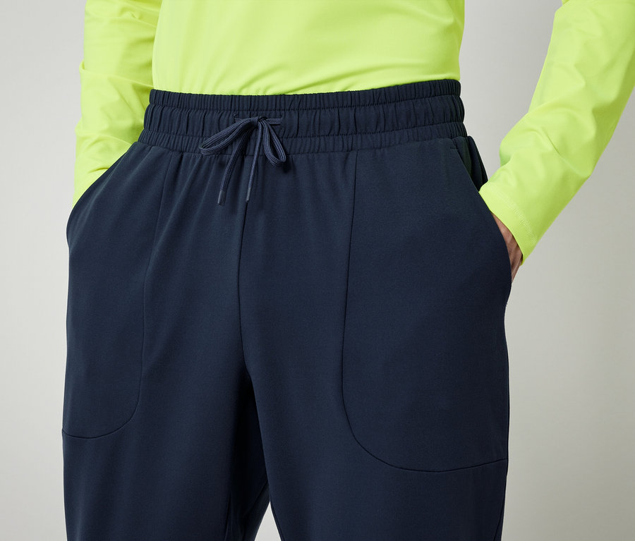 Osoba v neonově zelené košili a tmavě modrých kalhotách s rukama v kapsách.