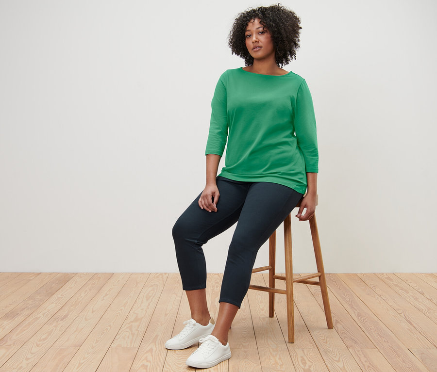 Žena sedí na stoličce a má na sobě zelené tričko s tříčtvrtečním rukávem.
