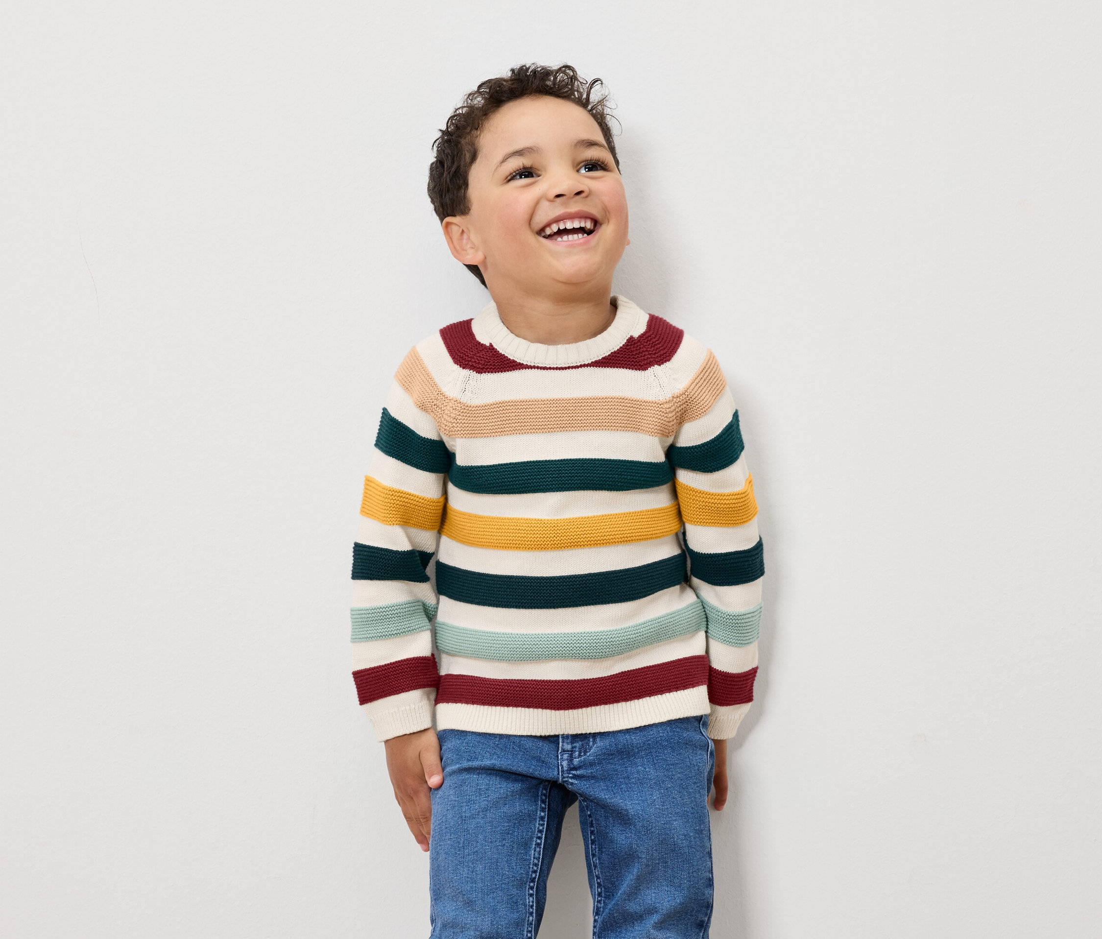 Chlapec se směje a má na sobě pruhovaný svetr a džíny.