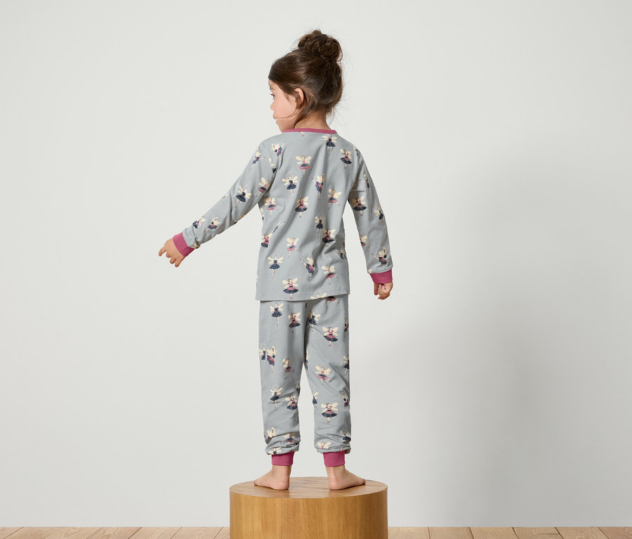 Dívka stojí zády, oblečená v šedém pyžamu s potiskem víl.