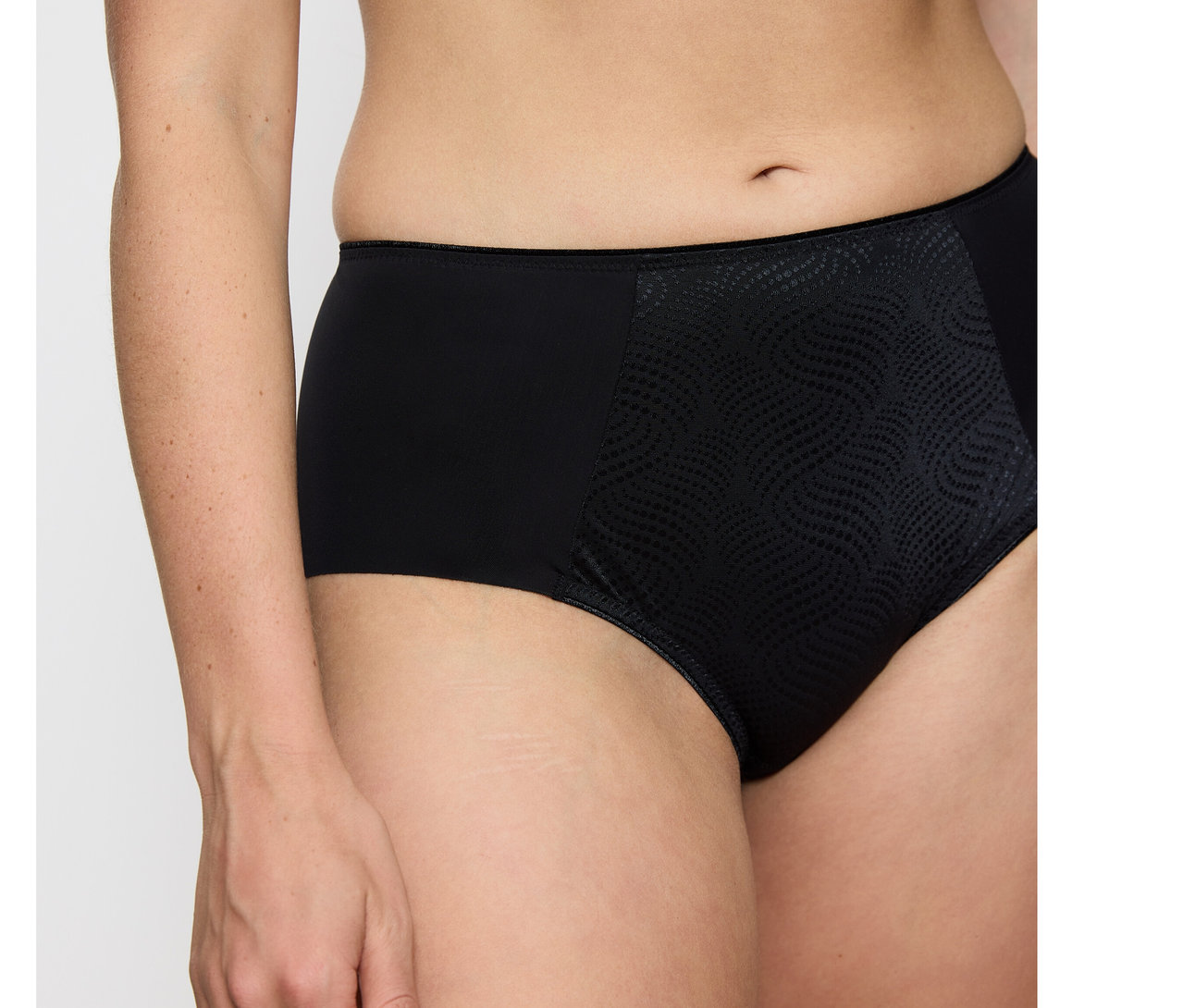 Osoba má na sobě černé zmenšující bokové kalhotky Triumph Essential Minimizer Hipster X s hladkými boky a texturovaným, vzorovaným předním dílem.