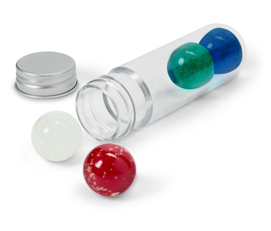 Průhledná tuba leží na boku s modrou a zelenou koulí uvnitř, stříbrné víčko vedle a bílá a červená koule venku.