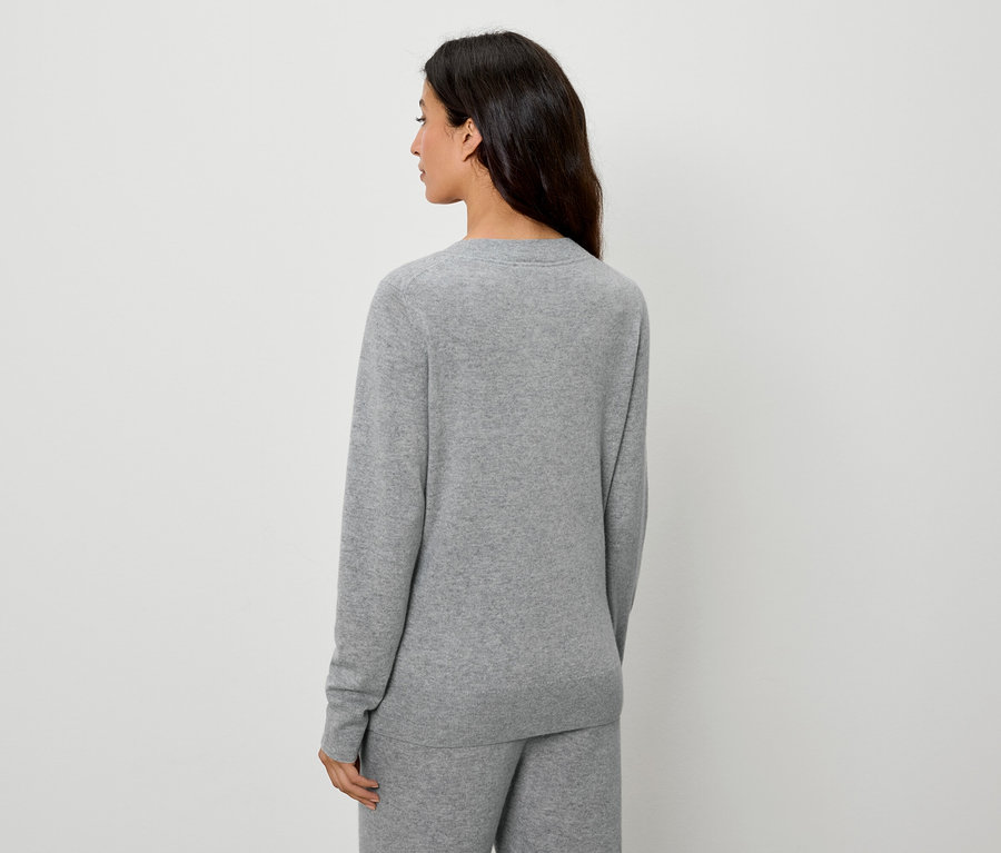 Zezadu pohled na ženu s tmavými vlasy v šedém svetru a kalhotách.