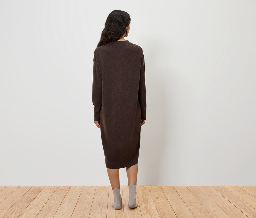 Žena stojí zády k fotoaparátu a má na sobě hnědé šaty a šedé ponožky.