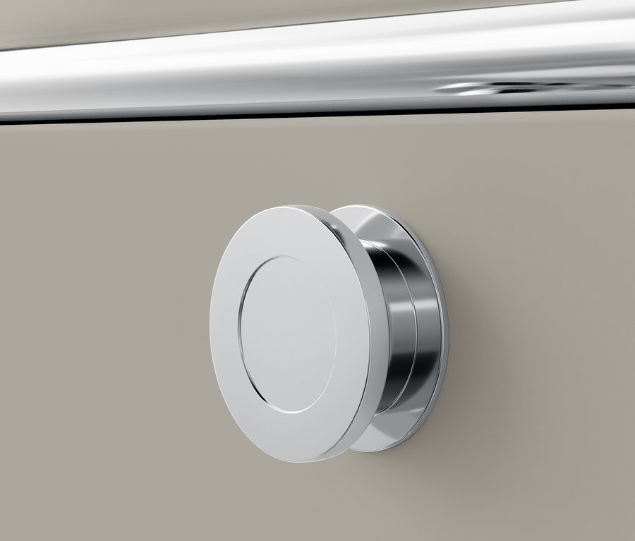 Detail chromové kulaté úchytky na béžové zásuvce.