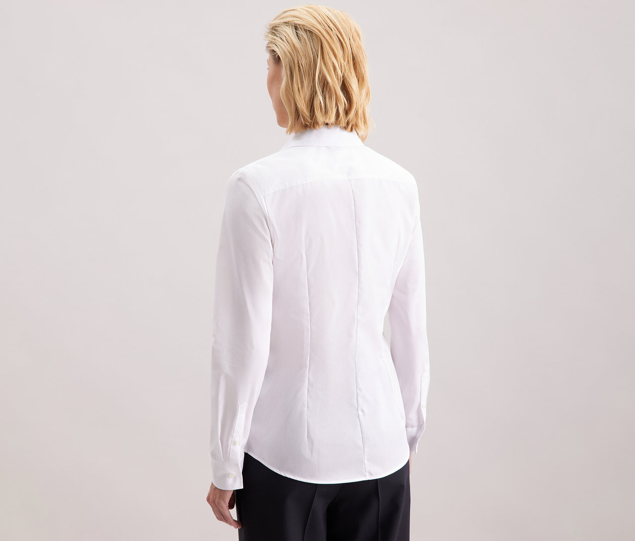 Pohled zezadu na blondýnu s vlasy po ramena v bílé halence Seidensticker Slim Fit non iron.