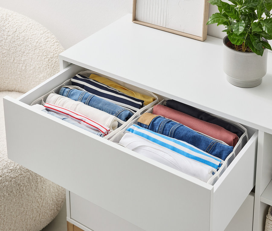 Otevřená zásuvka bílé komody obsahuje úhledně složené oblečení v organizérech.
