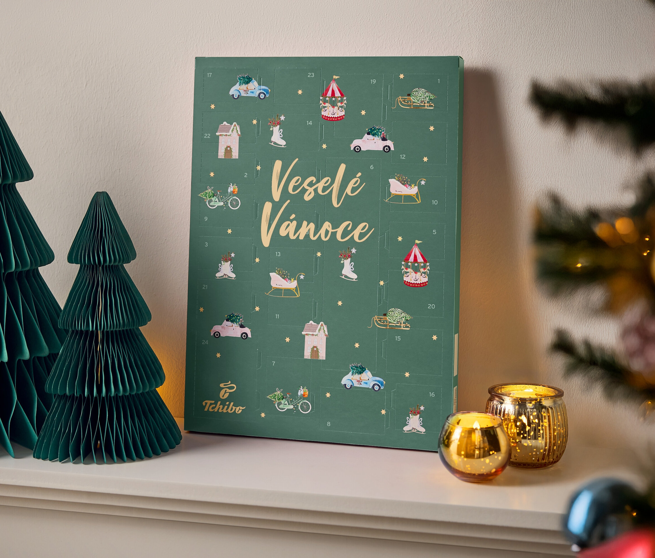Dva zelené papírové stromečky vedle zeleného adventního kalendáře s nápisem Veselé Vánoce a zlaté svíčky.