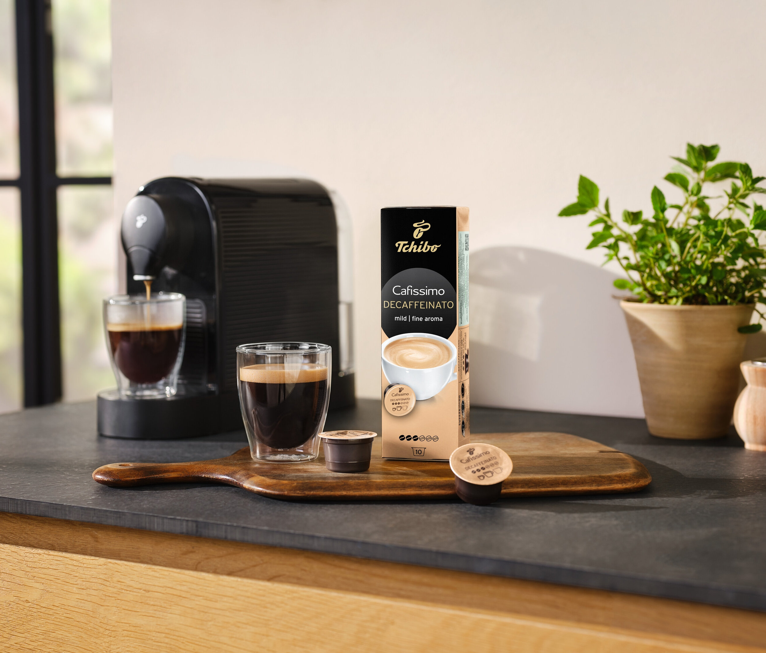 Kávovar nalévá kávu do sklenice vedle balení kapslí Cafissimo Decaffeinato.