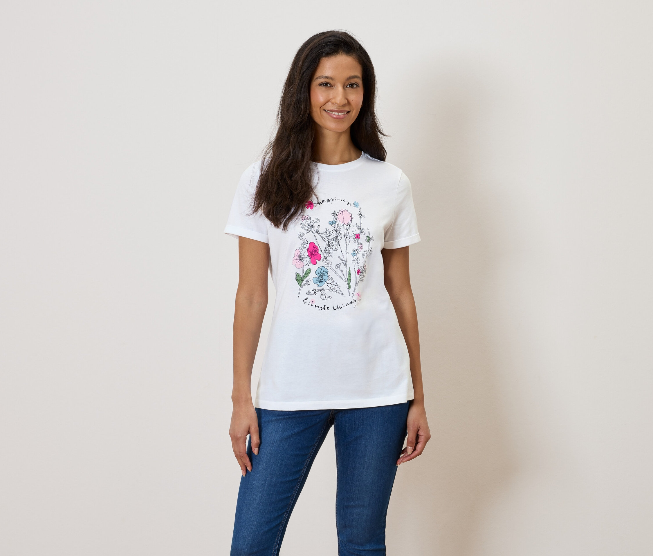 Žena má na sobě bílé tričko s květinovým potiskem a modré džíny.