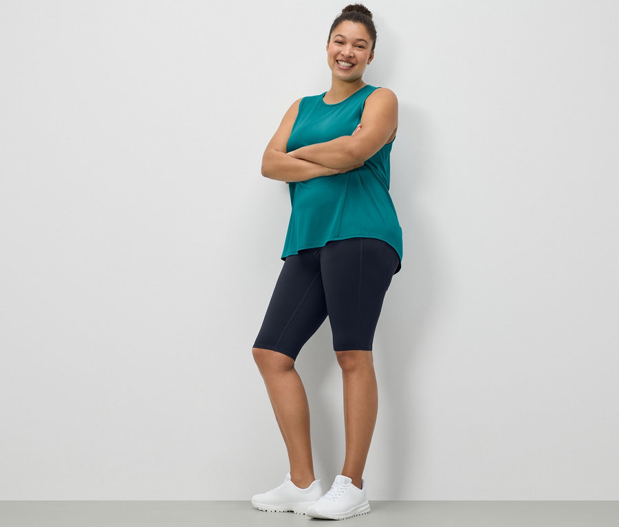 Žena pózuje ve sportovních cyklistických šortkách tmavě modré barvy a tyrkysovém sportovním topu z dvoudílné sady.