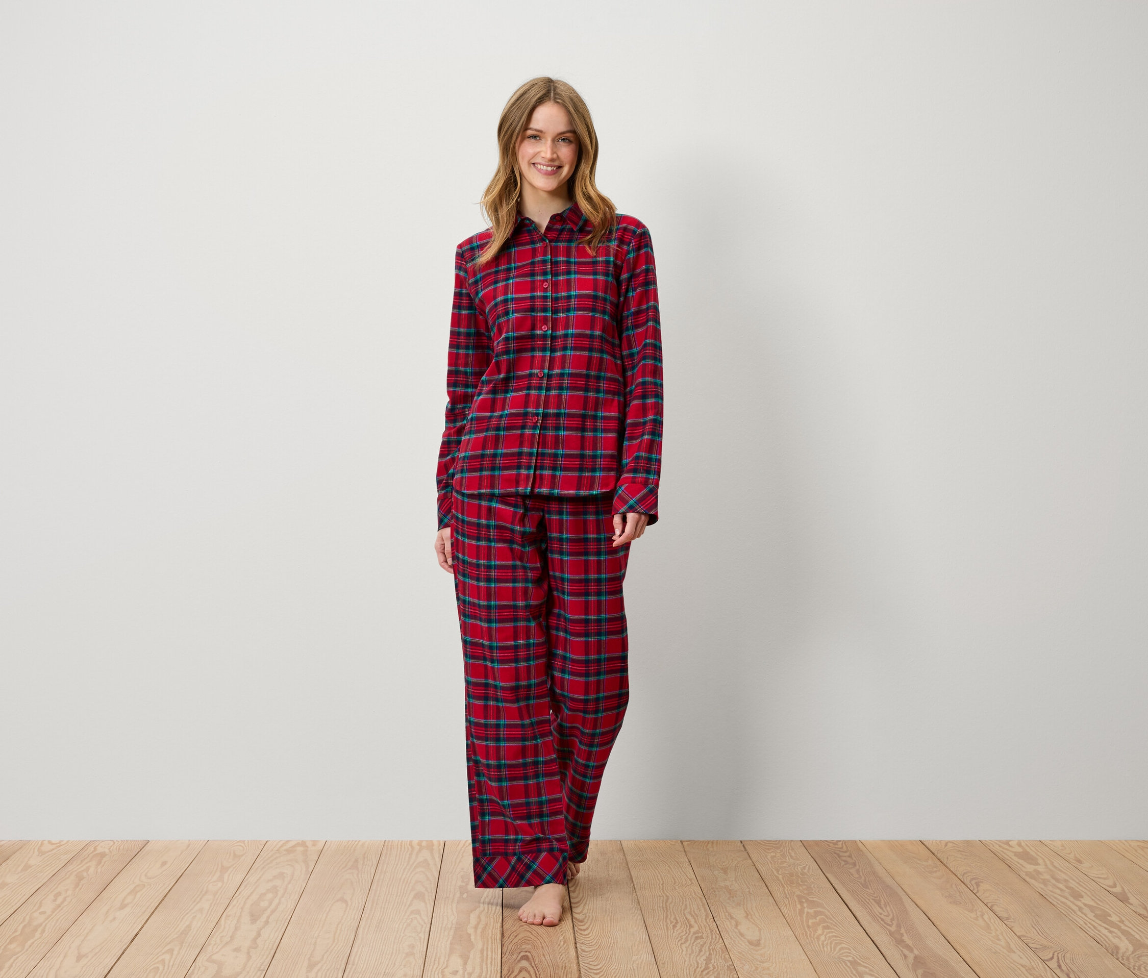Žena stojí a usmívá se, oblečená v červeném kostkovaném pyžamu.