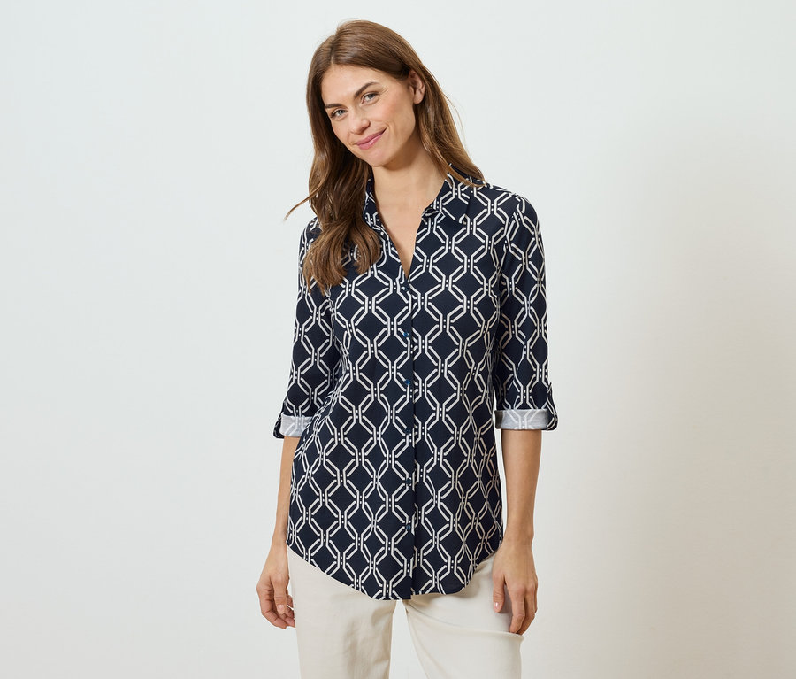 Žena má na sobě tmavě modrou halenku s bílým geometrickým vzorem a béžové kalhoty.