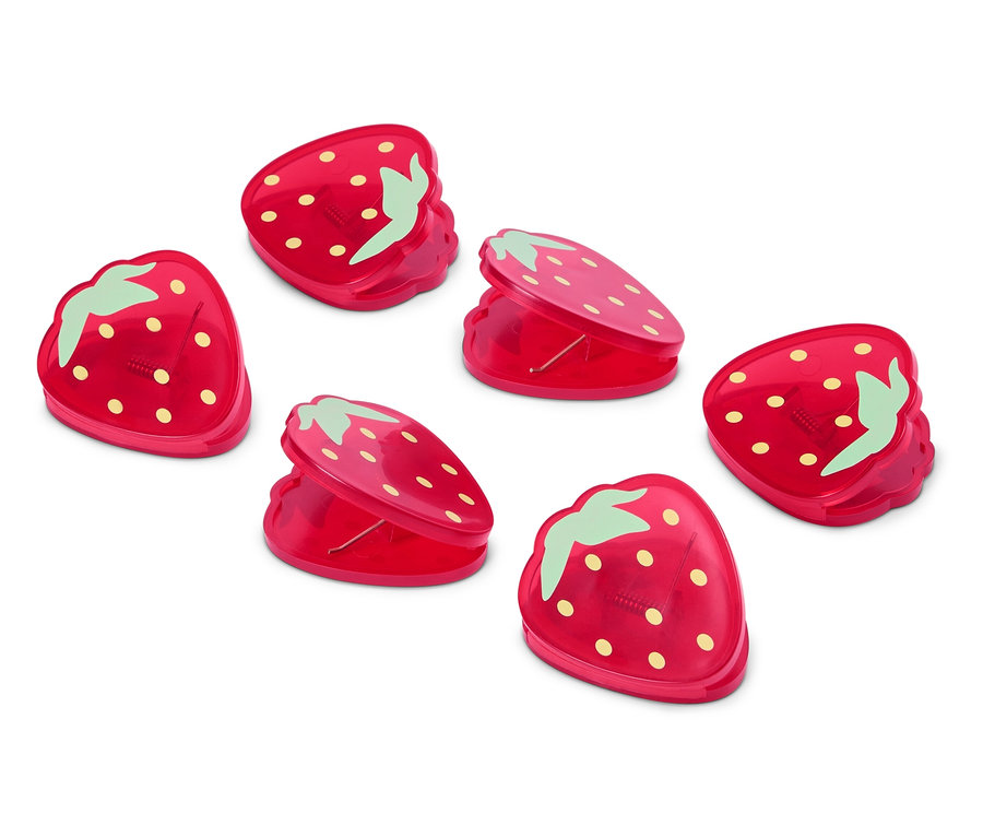 Šest červených sponek ve tvaru jahod leží na bílém povrchu.