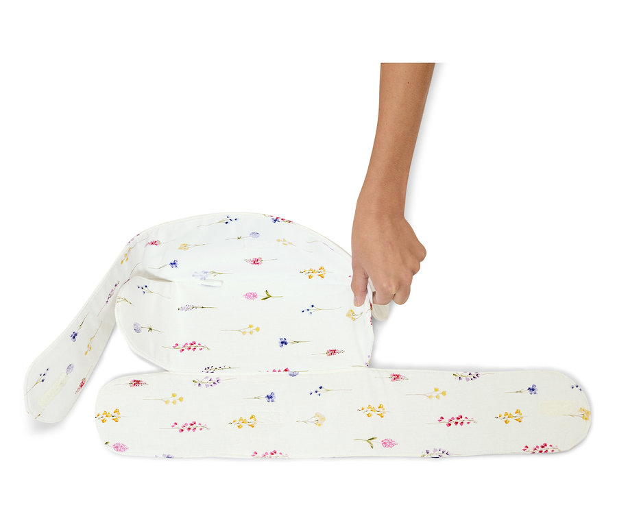 Ruka skládá bílý kojící polštář s květinovým vzorem.