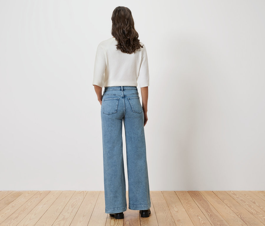 Žena stojí zády ke kameře a má na sobě světlou blůzu a široké džíny.