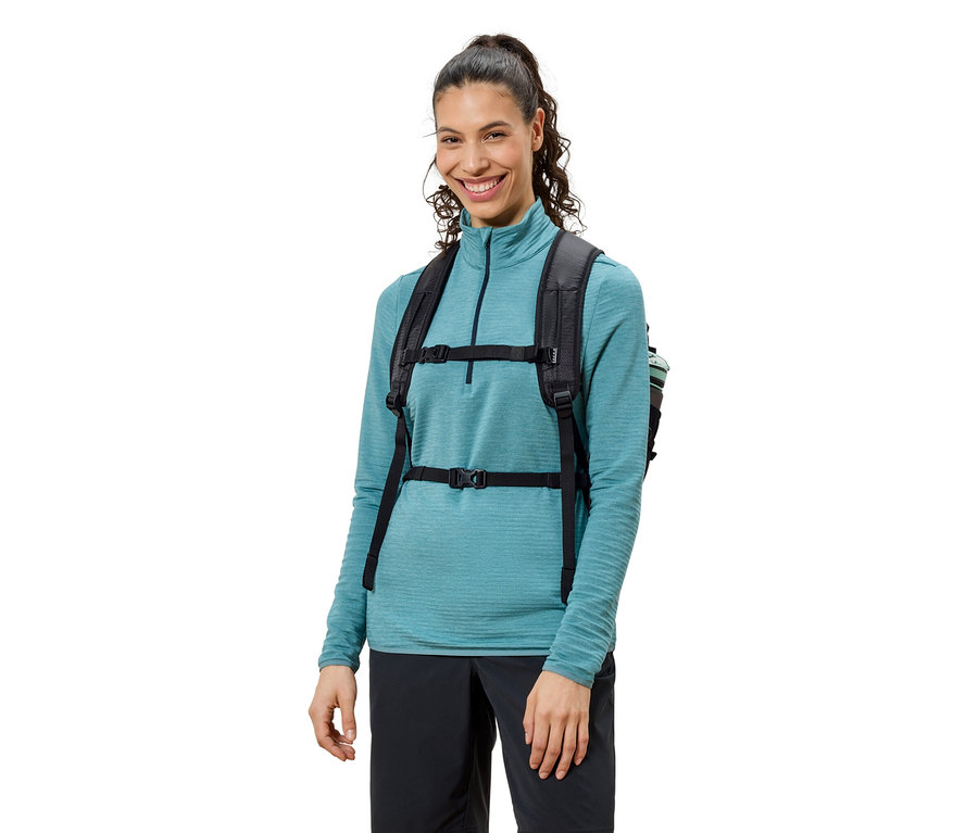 Usmívající se žena s černým batohem, modrým topem a černými kalhotami.